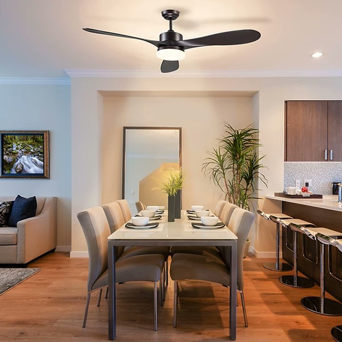 A modern dining area with a black ceiling fan and light, featuring a rectangular dining table, beige chairs, and a cozy living room in the background.